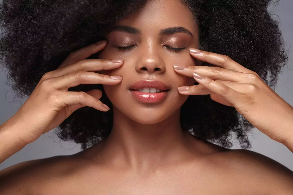 femme métissée au yeux fermés qui se touche le visage pour illustrer l'article qui traite de la definition glow