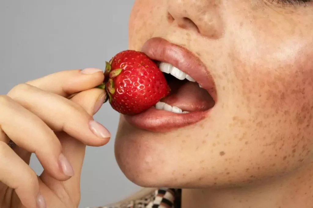 Teint terne malgré vos soins ? 7 erreurs qui tuent l’éclat 2 Femme qui mange une fraise pour illustrer l'article "teint terne : 7 raisons"